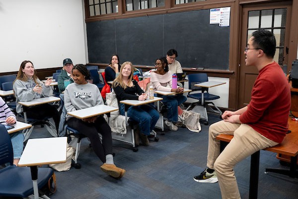 Professor sitting on desk in front of class