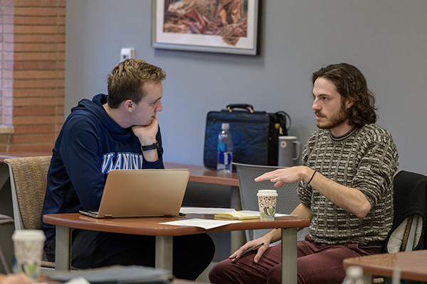 Students talk together at a table with a laptop open on it.