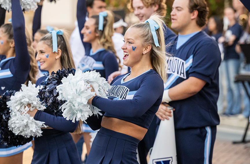 A group of Villanova cheerleaders wave pom-poms outside on campus. 