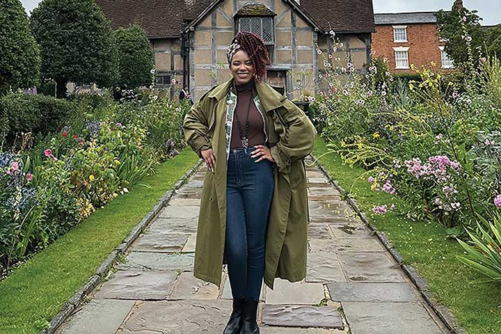 Taahira Davis looking stylish while standing on a slate pathway surrounded by wildflowers, in front of an old-looking cottage in England.